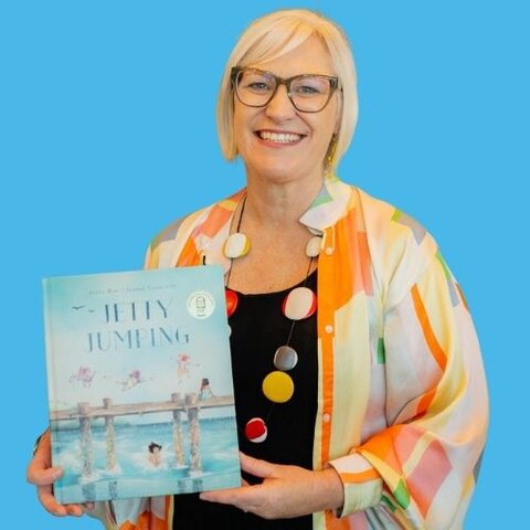 The author, Andrea Rowe, holding the children’s book Jetty Jumping against a bright blue background.